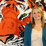 Melissa stands near tiger mural, smiling.