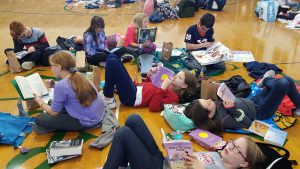 photo shows boys and girls laying and sitting on gymnasium floor reading books