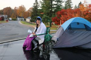 photo shows woman wrapped in blankets seated in camp chair next to tent