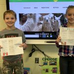 photo shows two kids holding papers up smiling