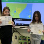 photo shows two kids holding papers up smiling