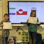 photo shows two kids holding papers up smiling