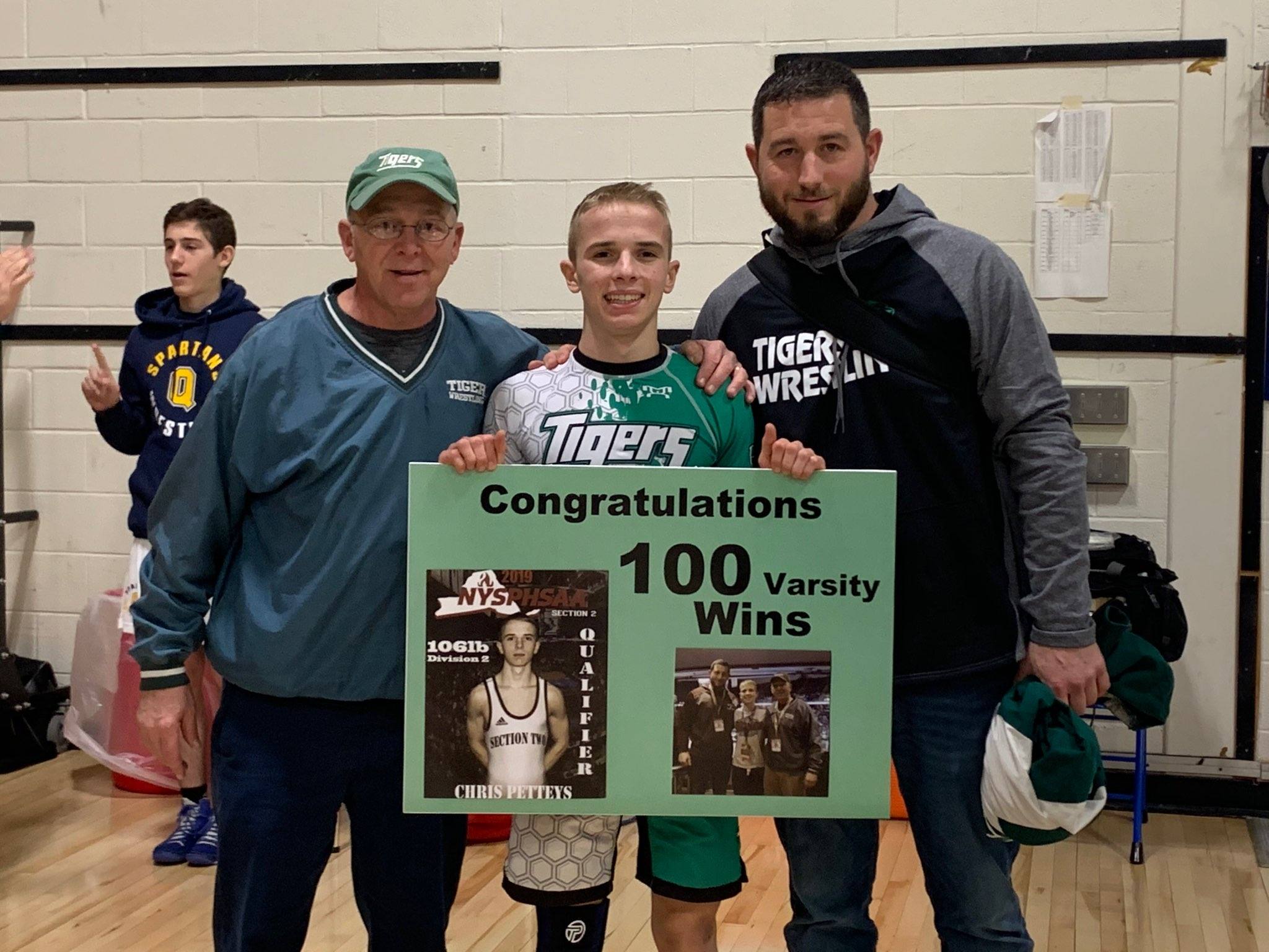 HFHS wrestler Chris holds a poster commemorating his 100th win; he's flanked by his two coaches