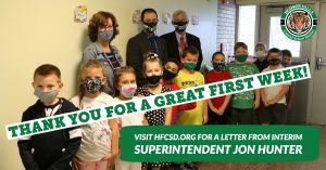 photo shows children lined up with masks smiling at camera inside school