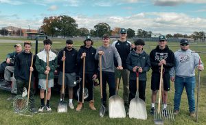 photo shows group of boys outside holding gardening tools and smiling