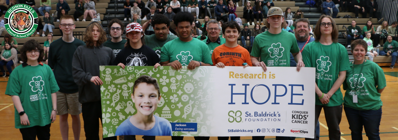 Photo of 13 individuals posing with a research is hope banner for St. Baldricks foundation